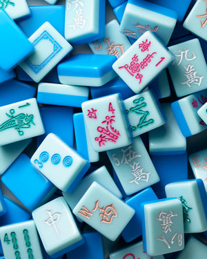 A close-up, top-down view of multiple light blue and medium blue mahjong tiles with colorful Chinese characters and symbols, filling the entire frame.