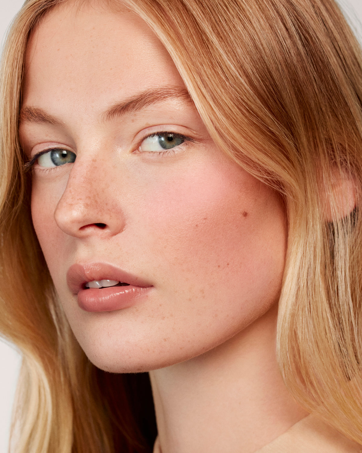 Blonde model wears the Baby Cheeks Powder Blush Duo in Coquette / Mimi. 
